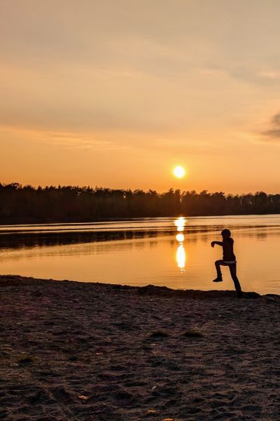 See bei Sonnenuntergang, im Vordergrund ein fröhlich springender Junge