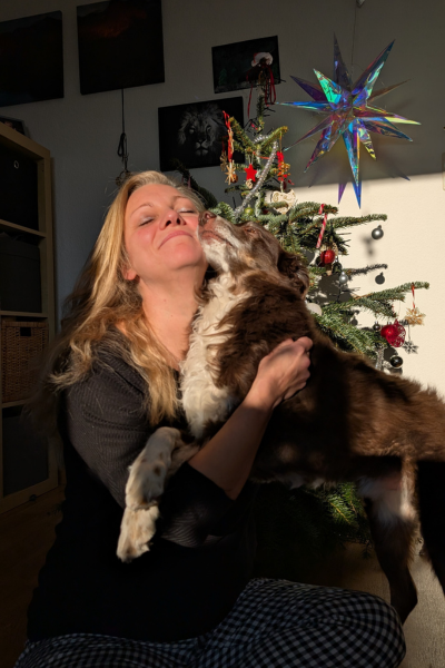 blonde Frau und brauner Hund kuscheln vor Weihnachtsbaum