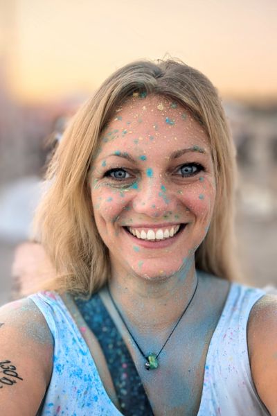 Blonde Frau mit bunter Farbe besprengelt während eines Holi Colour Festivals